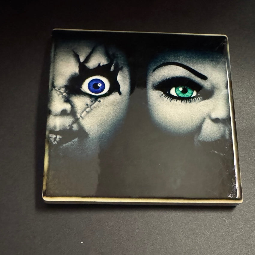 Square ceramic horror coaster featuring two eerie faces side by side with vivid blue and green eyes